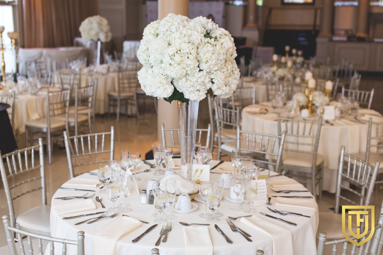 Hotel banquet ballroom set with round tables, chiavari chairs and white floral centerpieces, with no service staff in the room